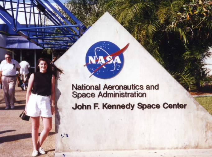 Tricia Royle posing at the sign at the entrance to Kennedy Space Center.